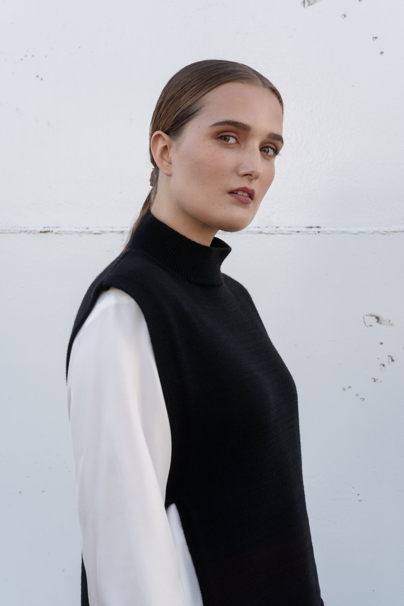 Woman wearing a black sleeveless top over a white shirt against a light gray background