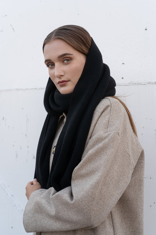 Woman wearing a black scarf and beige coat against a white background