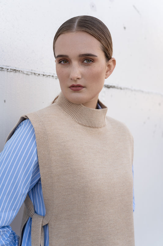 Woman wearing a beige knitted vest over a blue striped shirt against a white background