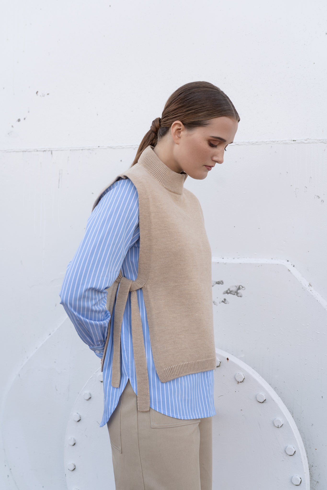 Woman wearing a beige vest over a blue shirt against a white background