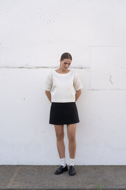 a model wearing white silk top and black silk mini skirt with white ankle socks.