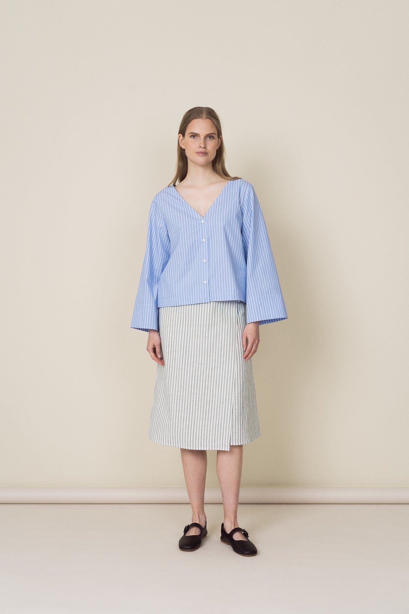The model is wearing a v-neck cotton shirt with light blue stripes and a linen wrap dress with faded green stripes.
