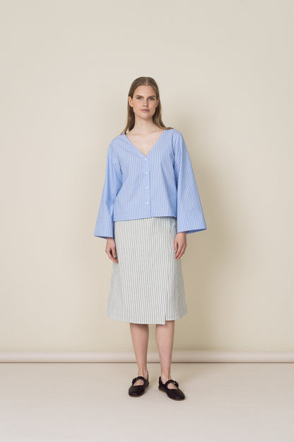 The model is wearing a v-neck cotton shirt with light blue stripes and a linen wrap dress with faded green stripes.