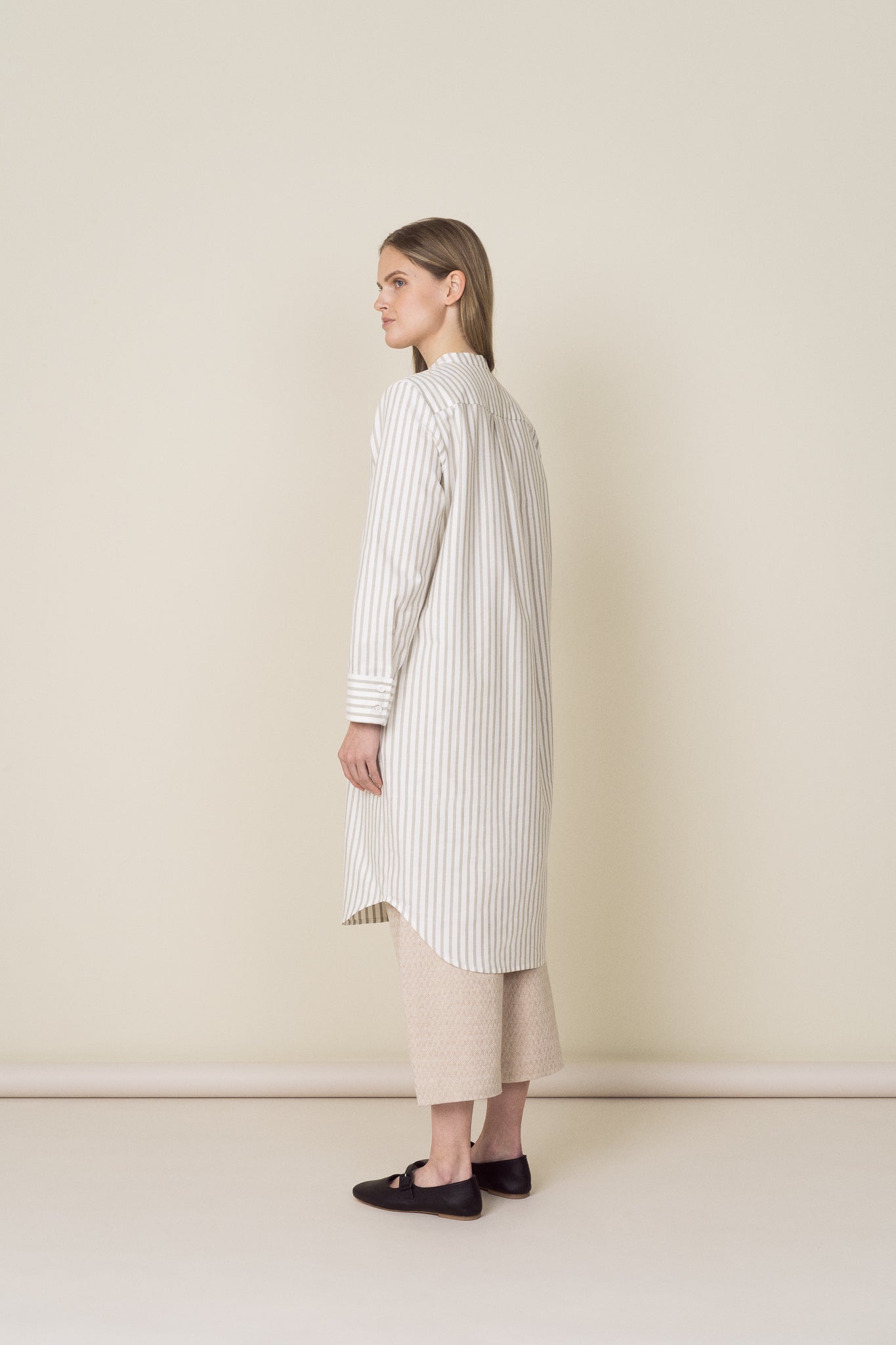 A model wearing a striped shirt dress layered over beige linen trousers.