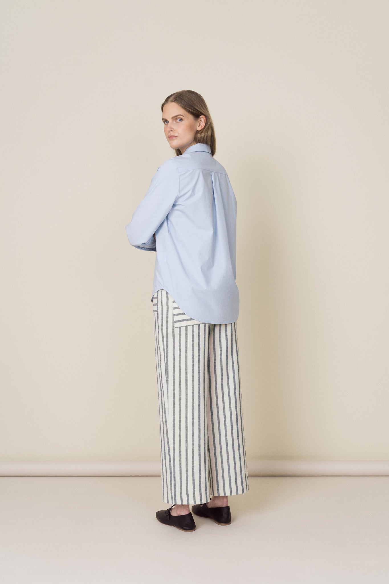 model wearing light blue cotton shirt and striped linen & cotton straight leg trousers